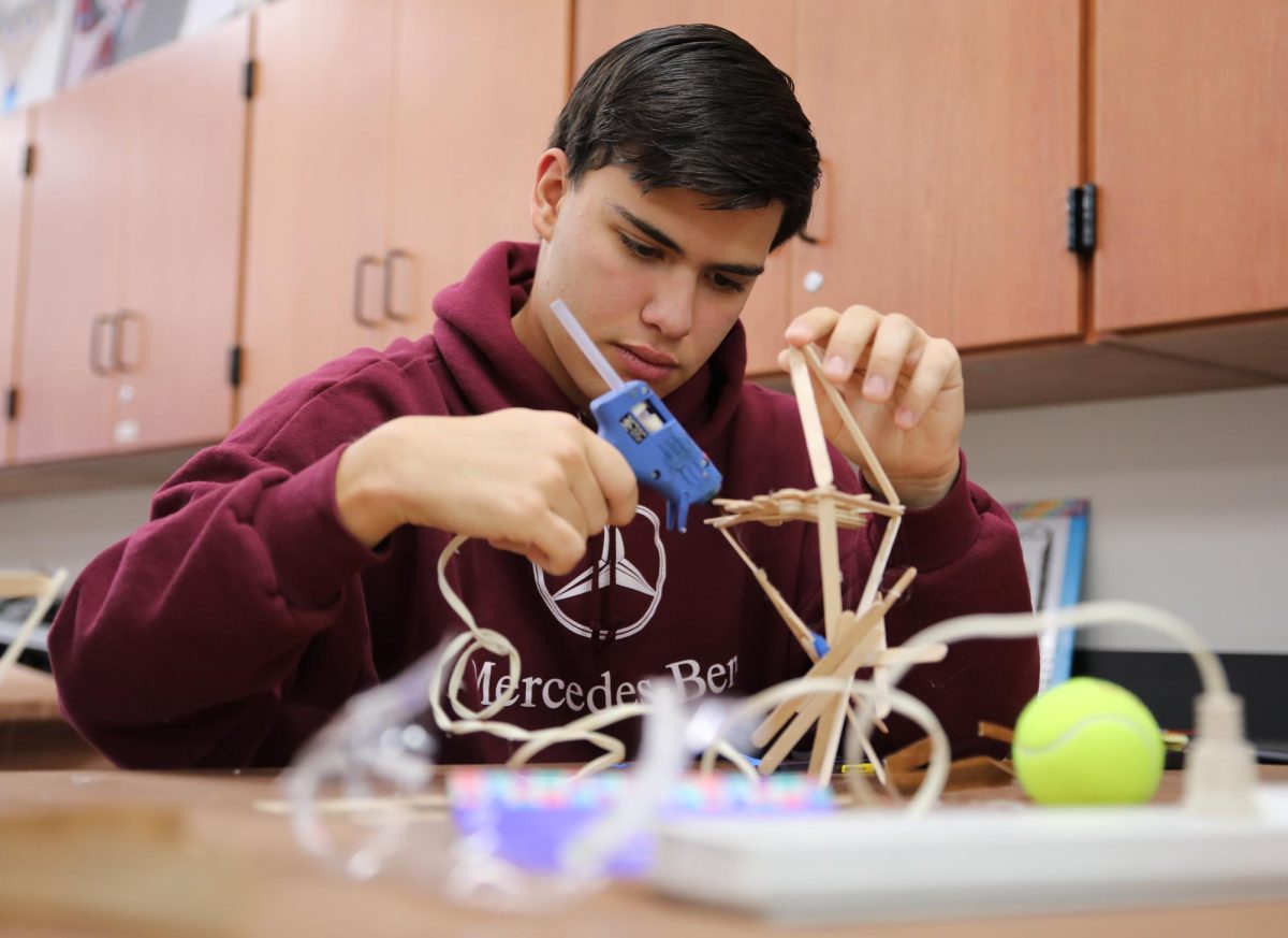 Focusing intently, senior Colin Reyes uses hot glue to build his physics structure for the egg drop Dec. 4. For the project, students were only allowed to use Popsicle sticks, glue and tape. "I enjoyed seeing it all come together and getting to be creative with the limited materials we had," Reyes said. "Although my egg ended up breaking, I still had a lot of fun making it."